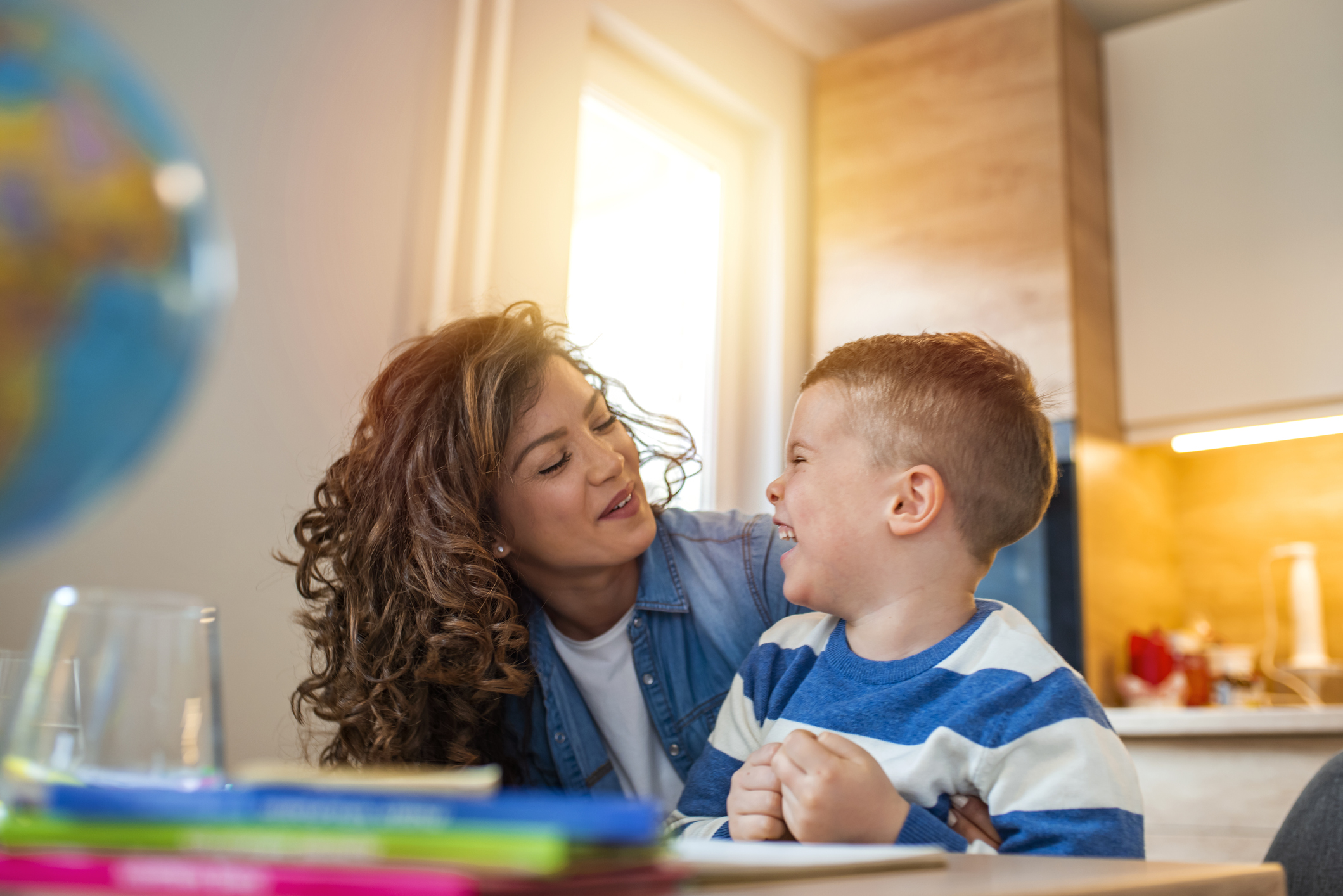 Kind mother helping her son doing homework in kitchen. Mother Helping Son With Homework At Table. Children's creativity. Portrait of smiling mother helping son with homework in kitchen at home