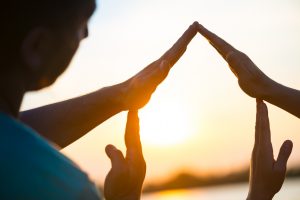 Young couple making a conceptual house symbol with hands against sunset. Real estate, housing, construction industry, architecture and design concept. Isolated with clipping path.