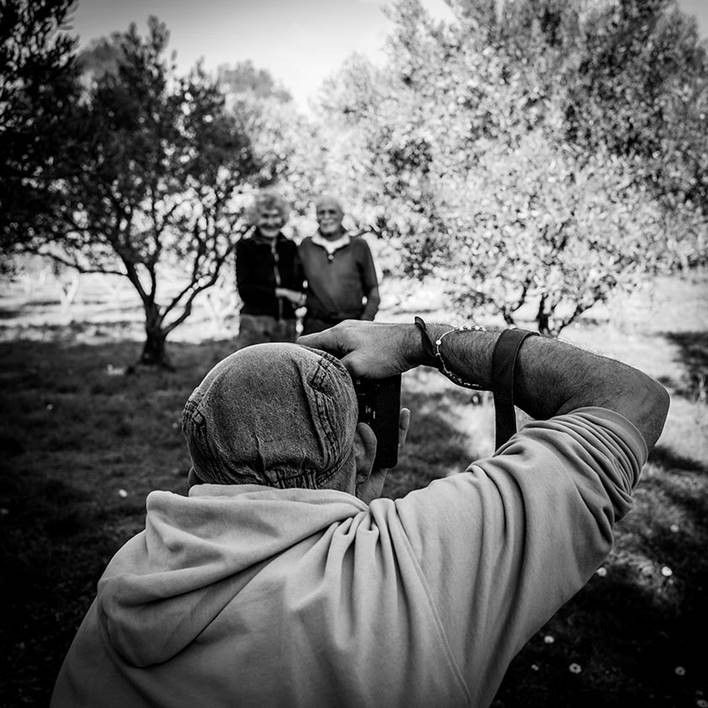 Photographe prenant une photo d'un homme et d'une femme près des oliviers en noir et blanc